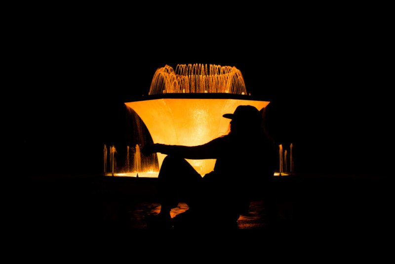 Silhouette einer jungen Frau vor einem beleuchteten Brunnen bei Nacht.