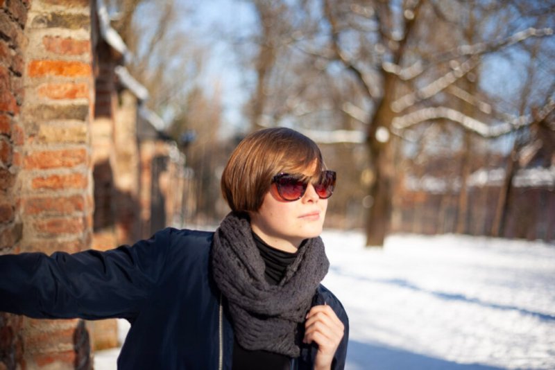 Fashion Shot: Junge Frau mit kurzen Haaren, Sonnenbrille und moderner Kleidung lehnt sich gegen eine Ziegelmauer.
