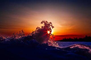 Foto einer Eisschicht, die von Sonnenstrahlen durchleuchtet wird, mit einem Sonnenuntergang im Hintergrund in warmen Orangetönen.