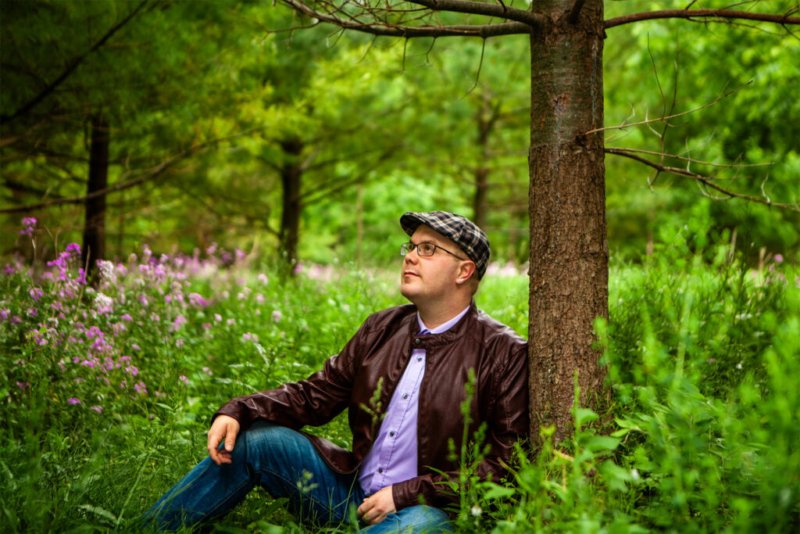Mann sitzt entspannt unter einem Baum in einem blühenden Wald.