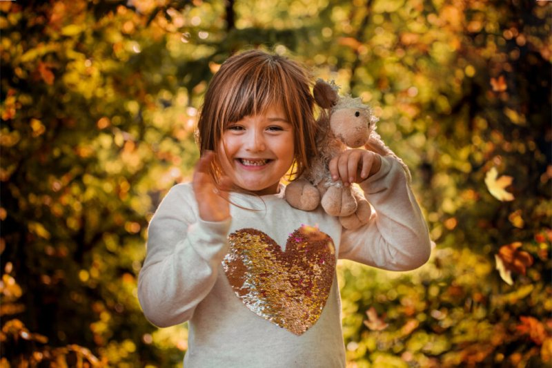 Porträt eines fröhlichen Mädchens mit Stofftier im Herbstwald.