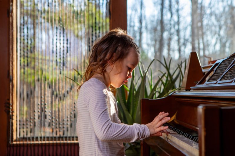 Junges Mädchen spielt Klavier in einem sonnendurchfluteten Raum mit Blick auf den Garten.