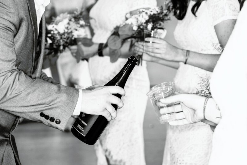 Moment der Freude bei einer Hochzeit, wo ein Mann in einem grauen Anzug eine Flasche Champagner öffnet und Gläser gefüllt werden.