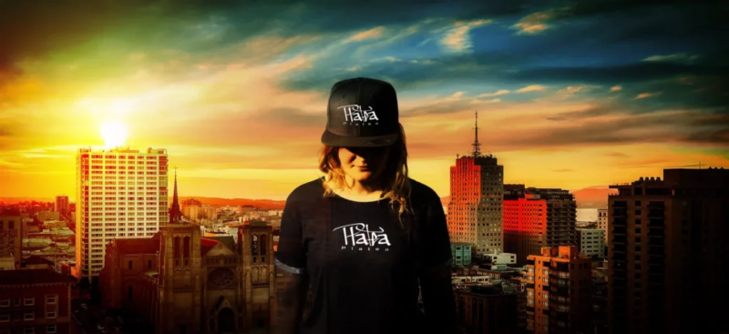 Branding-Banner der Mode-/Streetwear-Marke 'Platea' mit einer Frau, die ein Basecap und ein T-Shirt mit dem Markennamen trägt, vor einer urbanen Skyline bei Sonnenuntergang.