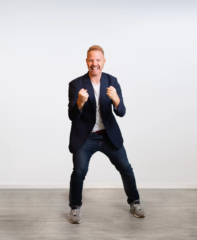 Brandingfoto eines Coaches, der in einem lässigen Outfit steht und motiviert die Fäuste ballt, vor einem neutralen Hintergrund.