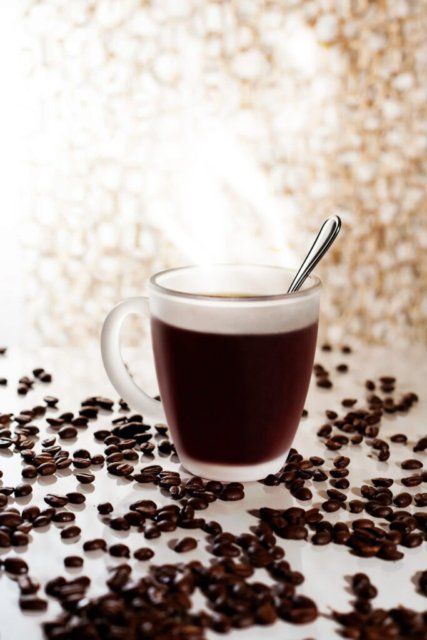 Dampfende Tasse Kaffee umgeben von gerösteten Kaffeebohnen.