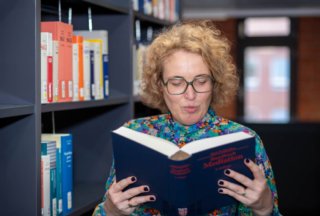 Professionelles Porträtfoto einer Frau beim Lesen eines Fachbuchs über Mediation in einer Bibliothek