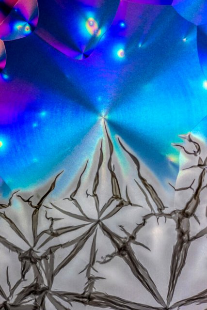 Farbenfrohe Kristalle bilden abstrakte Mikrostrukturen, die an eine Gebirgskette vor einem nachtblauen Hintergrund erinnern.